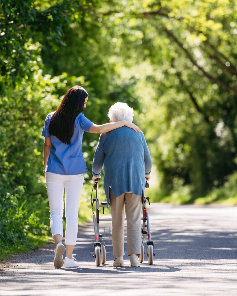 Female Caregiver And Senior Woman With Walker On Walk In