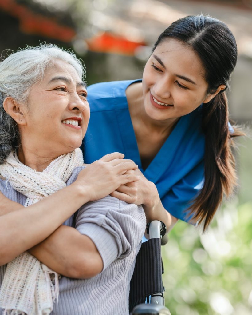 Compassionate Asian Woman Provides Care To Elderly Person In Wheelchair